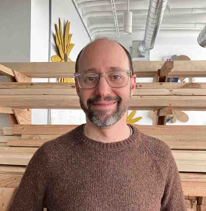 reDiscover Center Exe3cutive Director Jonathan Markowitz Bijur smiles against the background of a maker studio.