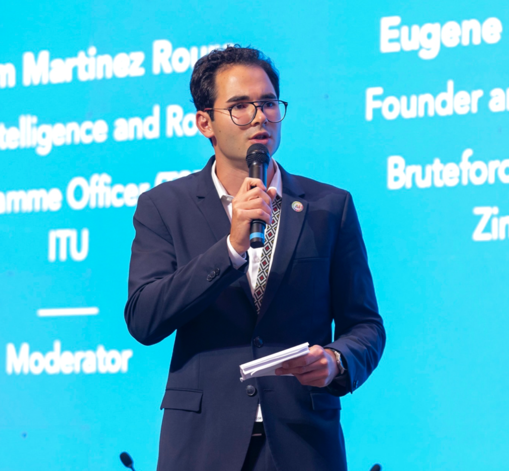 Guillem Martinez Roura speaks onstage in front of a blue background with white lettering,