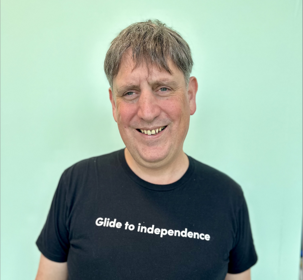 Glidance FOunder and CEO Amos Miller smiles as he sports a black T-shirt with "Glide to independence" on it in white lettering.