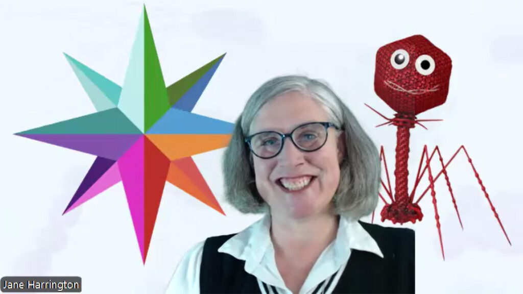 MedMicroMaps Founder and CEO Dr. Jane Harrington smiles in front of a screen showing her mascot, Phage.i, and her compass as we discuss microbiology.