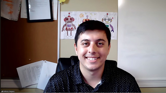 True Robotics President and Founder Anthony Galgano smiles against a background of a cork board on which are three students' drawings of robots.