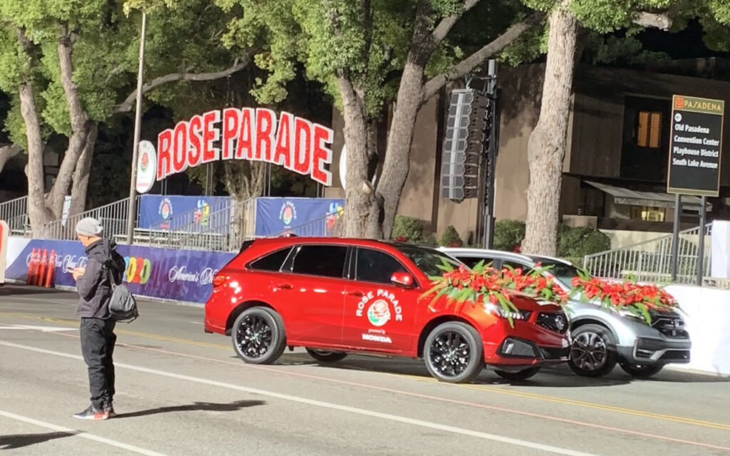 Rose Parade pace car and sound car await the parade near a "Rose Parade" sign