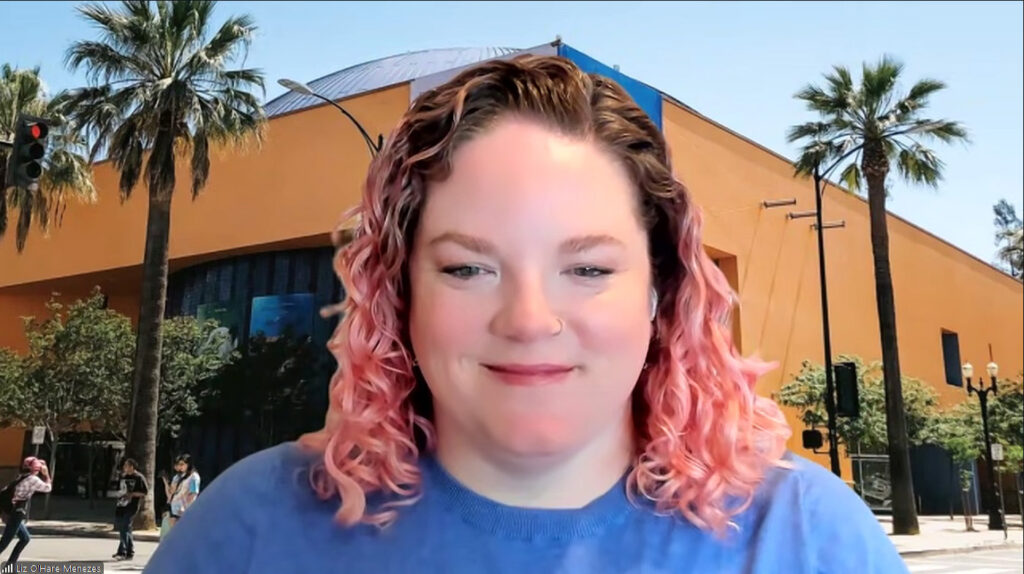 Summer Camps Program Manager Liz O'Hare smiles against a Zoom background of a photo of The Tech Interactive museum in San Jose.