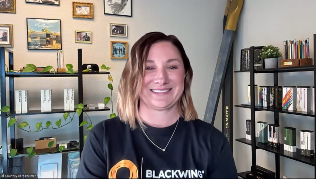 Blackwing Foundation Program Direcotr Courtney Berolzheimer smiles against a background of booshelves and paintings on her wall.