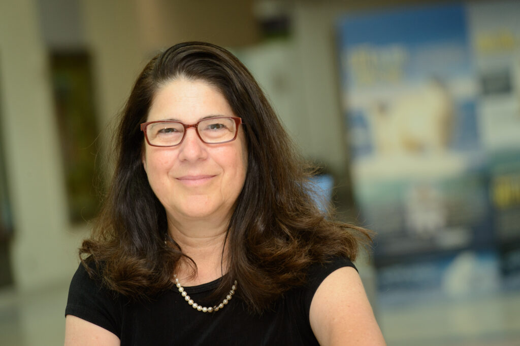 California Science Center Senior Vice President for Exhibits Diane Perlov smiles against a blurred background of museum exhibits.