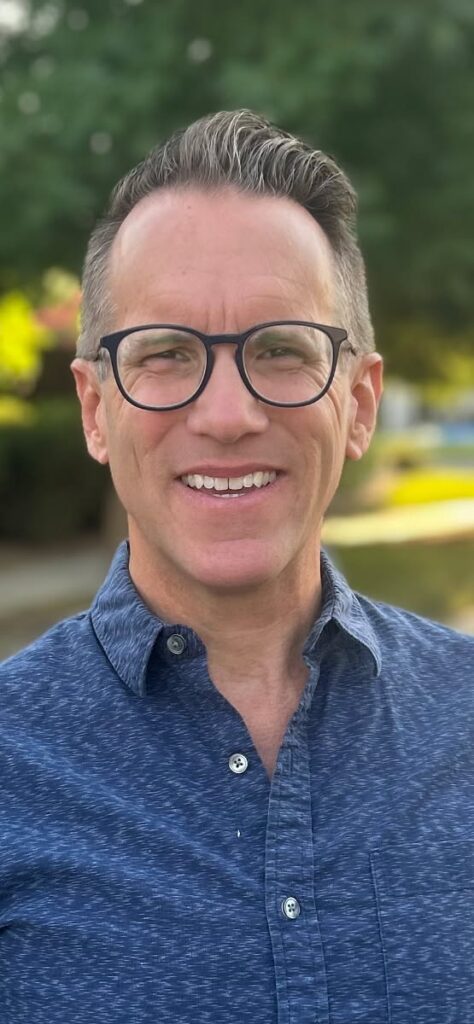 Fresno County Office of Education Director of STEM Education and Early Math, Office of the Fresno County Superintendent of Schools, Jonathan Dueck smiles against a background of a suburban street.