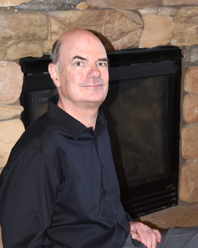 Author Matt Bille, co-author of The First Space Race, smiles next to a stone fireplace.